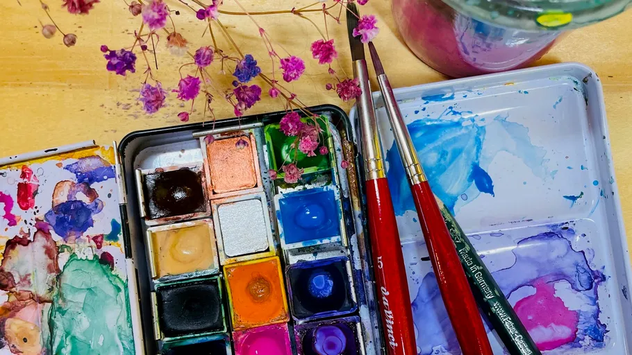 Paintbox, brushes, flowers on wooden table.