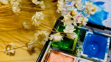 Getrocknete Blumen neben Aquarell-Farbpalette.