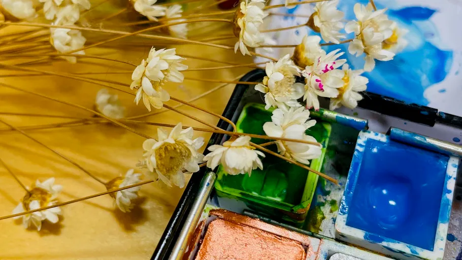 Dried flowers beside watercolor paint palette.