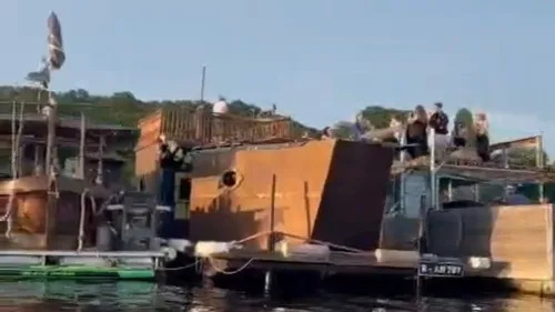 People standing on docked houseboat on water.
