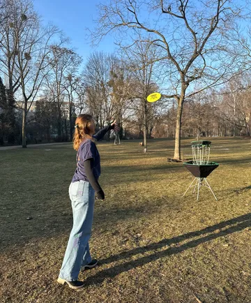 Person wirft Frisbee zu einem Discgolf-Korb.
