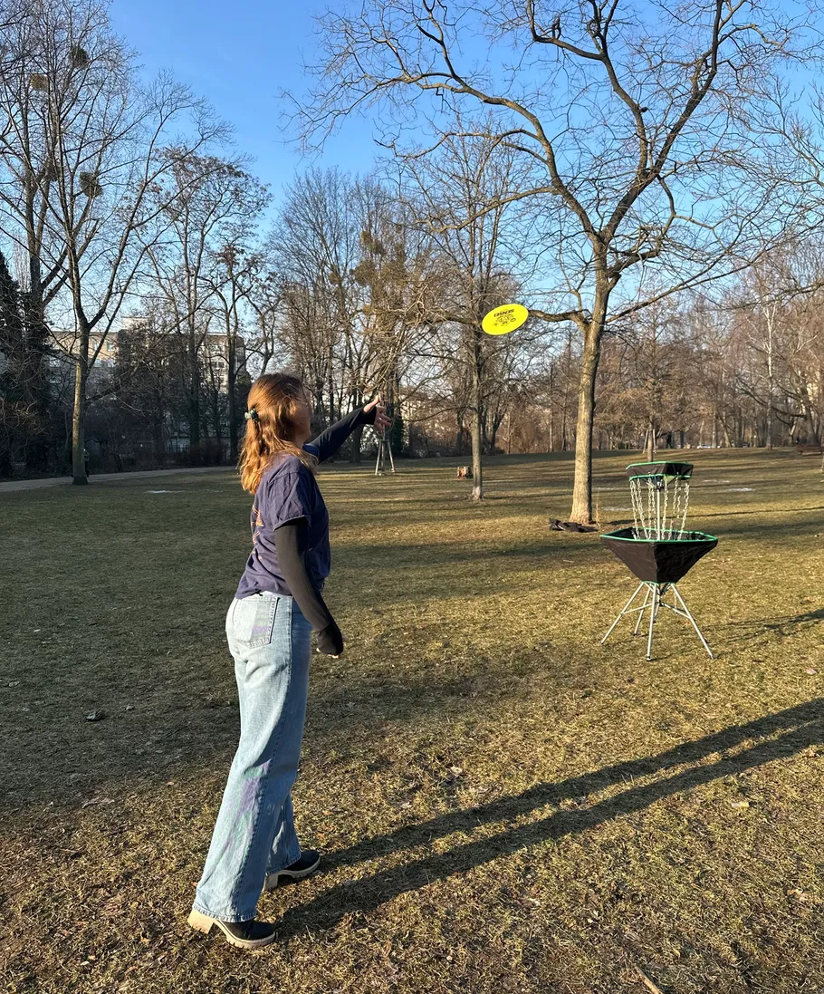 Person throwing a frisbee towards a disc golf basket.