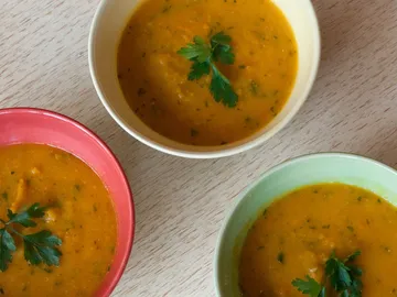 Drei Schalen mit gelber Suppe auf hellem Tisch.