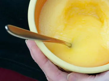 Gelbe Creme in einer Schüssel, Löffel rührt darin.