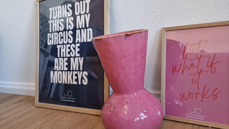 Pink vase beside framed quotes on floor.