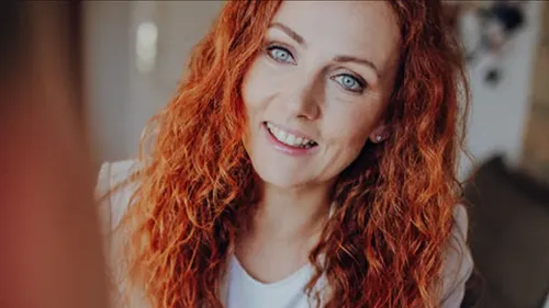 Woman with curly red hair smiling indoors.