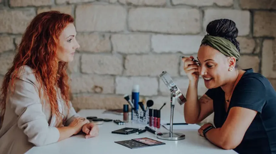 Two women sitting at a makeup table.
