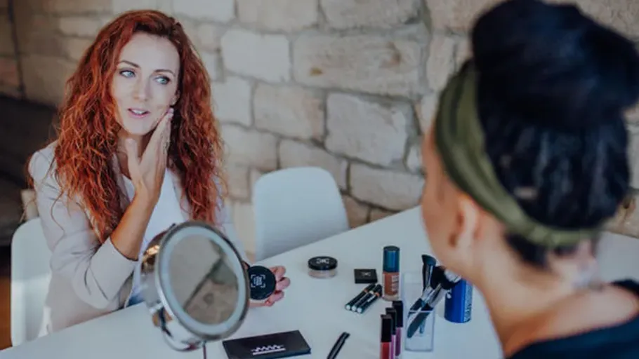 Two women discussing makeup at a table.