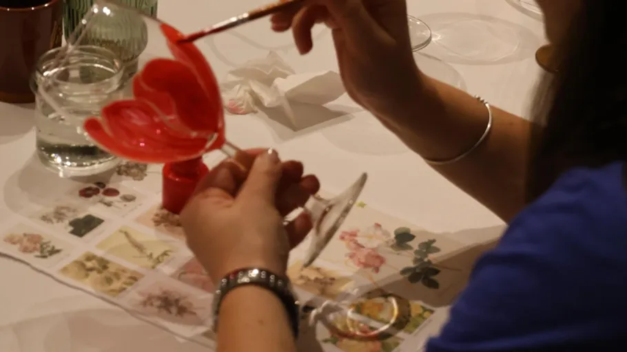 Person painting wine glass with red brush.