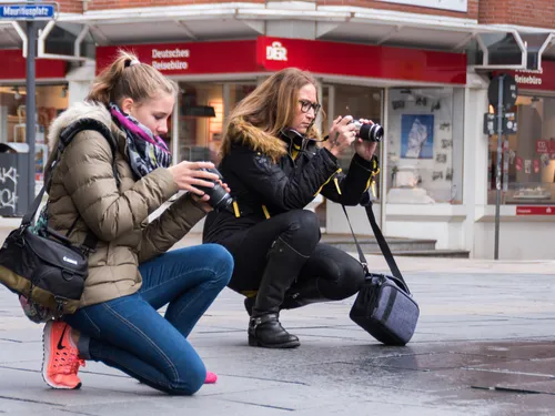 Zwei Frauen fotografieren knien auf dem Gehweg in der Stadt.