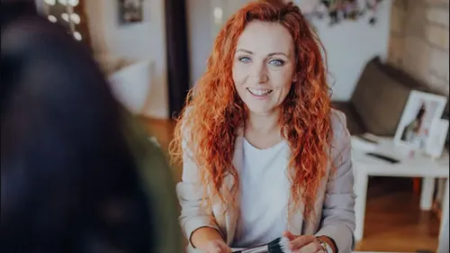 Lächelnde Frau mit roten Haaren hält Farbmuster.