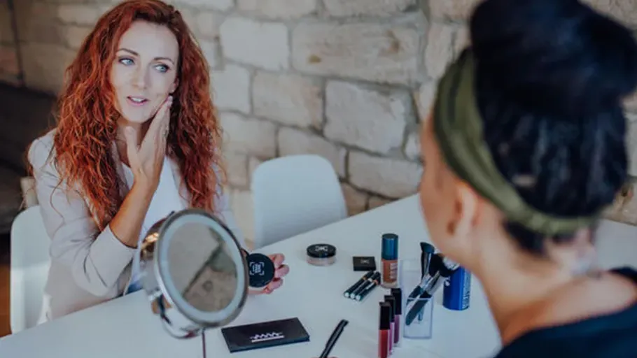 Two women applying makeup at a table.