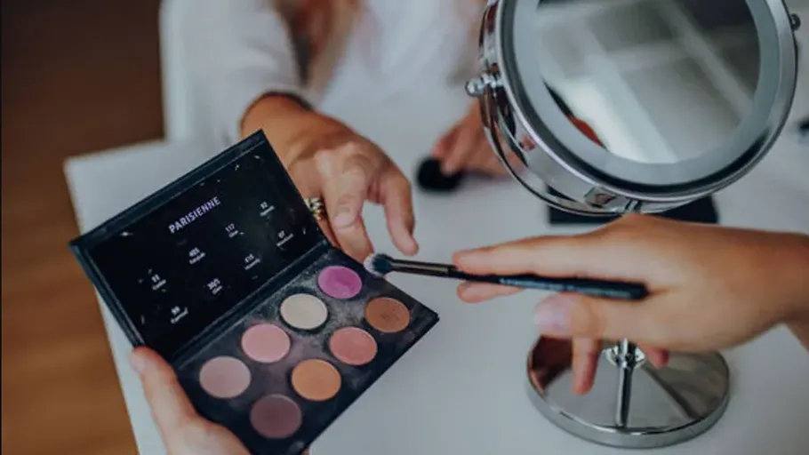 Hands hold makeup palette near mirror.