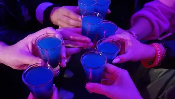 Hands holding blue shots in dim lighting.