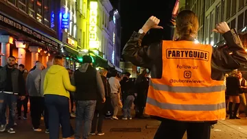 Party guide pointing at jacket in crowded street.