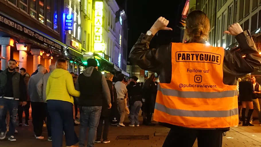 Partyguide zeigt auf Jacke in belebter Straße.