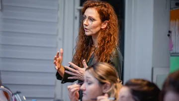 Woman gestures while speaking in a classroom.
