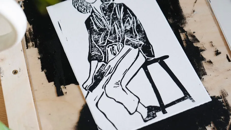 Monochrome linocut of person sitting on stool.