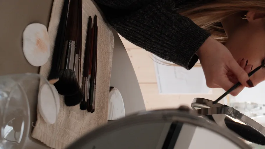 Woman applying makeup at vanity table.