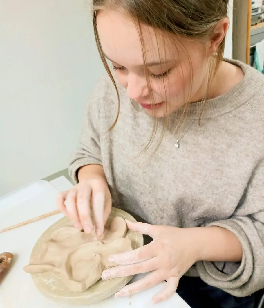 Woman sculpting clay on table indoors.