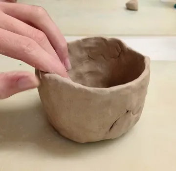 Hand shaping clay bowl on table.