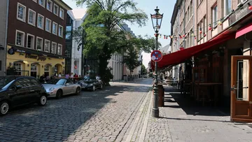 Leere Kopfsteinpflasterstraße mit geparkten Autos, sonniger Tag.