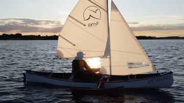 Person segelt kleines Boot bei Sonnenuntergang.