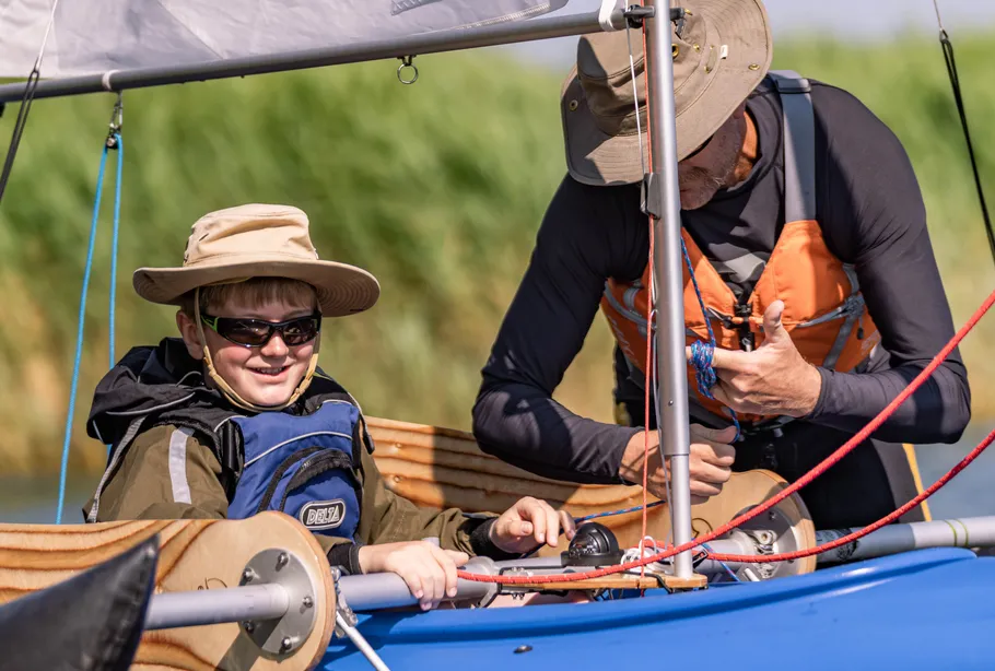 Junge und Mann segeln Boot, sonniger Tag.