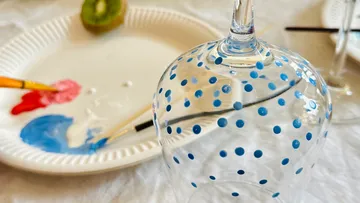 Bemaltes Glas mit blauen Punkten auf Tisch.