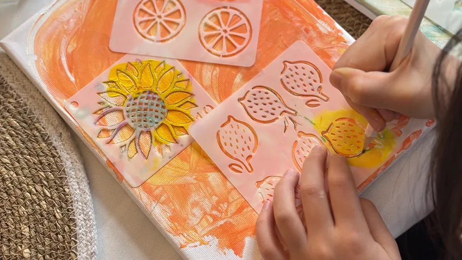 Hands stenciling fruit shapes on canvas.