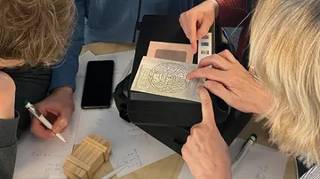 Personen lösen Rätsel mit Papieren und Gerät.