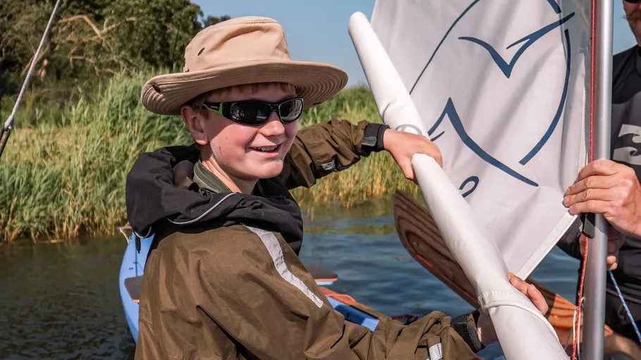 Boy wearing hat sailing boat on water.