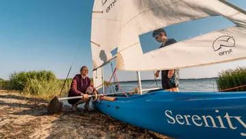 Two people rigging sailboat on sandy beach.