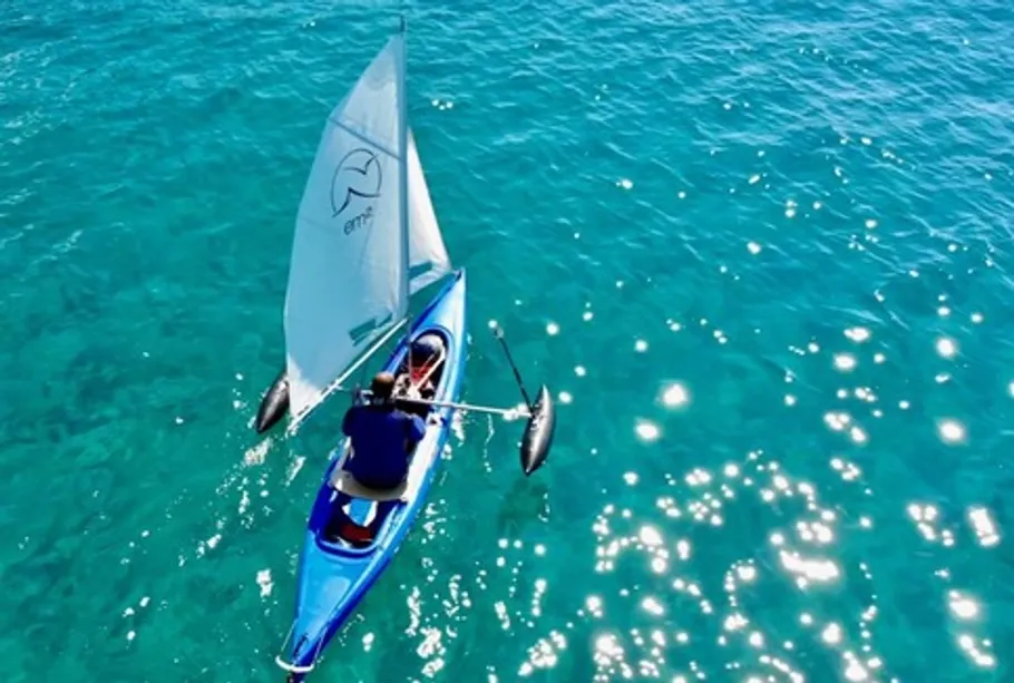 Kayak with sail on sparkling blue water.