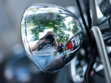 Reflective motorcycle shutter reflects people and nature in the background.