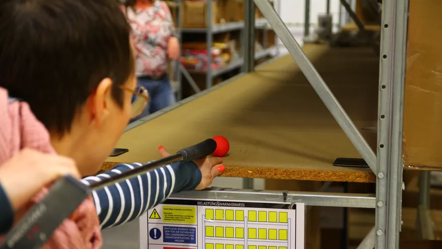 Person pointing tool at warehouse shelf.
