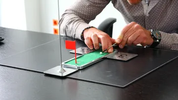 Mann spielt Minigolf auf Schreibtisch.