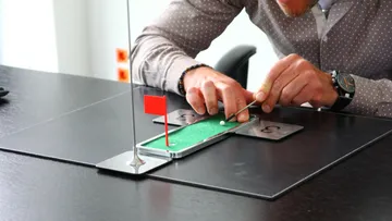 Person playing tabletop mini-golf on desk.
