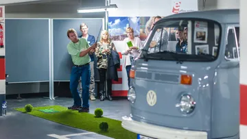 Mann spielt Minigolf drinnen, Zuschauer schauen zu.