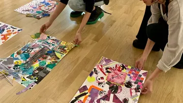 Zwei Personen arrangieren bunte Kunstcollagen auf dem Boden.