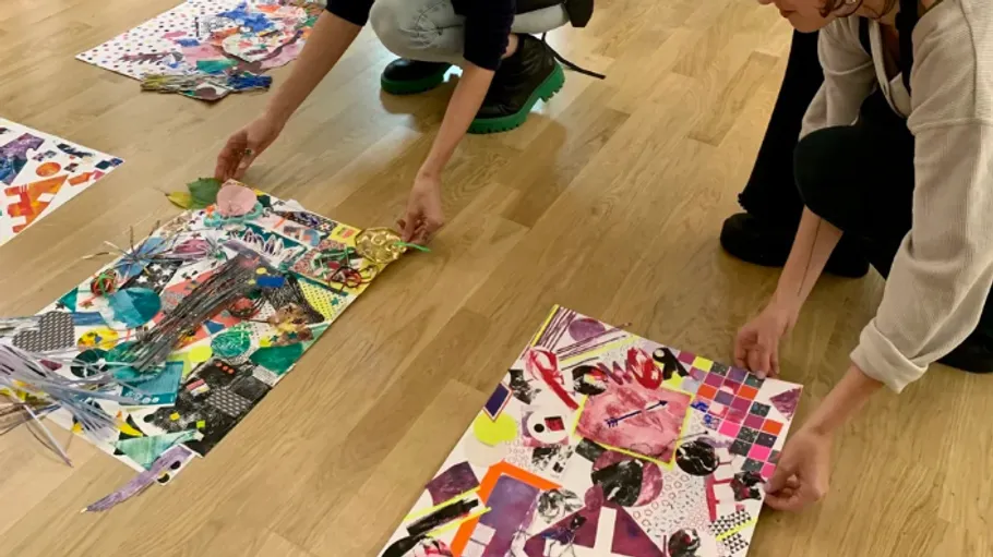Two people arranging colorful art collages on floor.