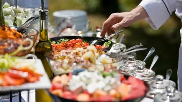 Hand selecting food from buffet table outdoors.
