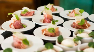 Prosciutto appetizers on white plates with greenery.