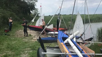 Menschen mit Segelbooten an grasiger Küste.