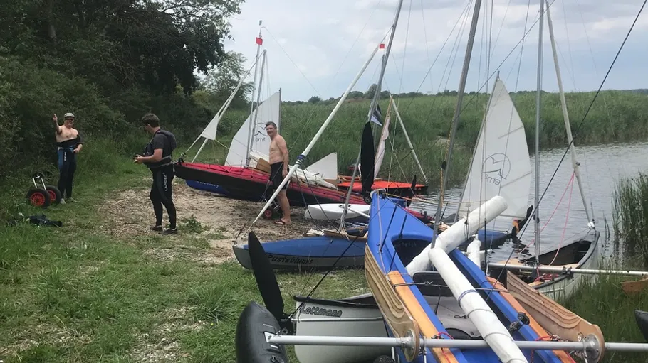 Menschen mit Segelbooten an grasiger Küste.