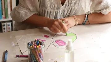 Person zeichnet mit Wachsmalstiften auf Papier.