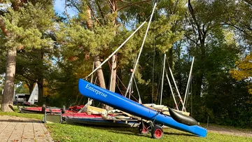 Blue sailboat named Enterprise on grassy area.