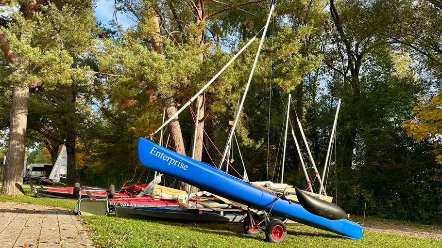 Blue sailboat named Enterprise on grassy area.
