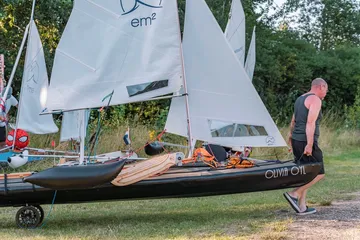 Mann zieht kleines Segelboot auf Grasfläche.