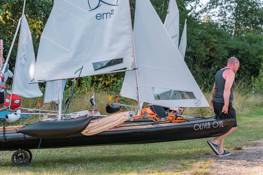 Mann zieht kleines Segelboot auf Grasfläche.